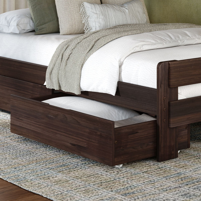 Dark walnut wooden trundle bed with under-bed storage drawer, white quilted bedding, beige knit throw and green accent pillows on a textured area rug