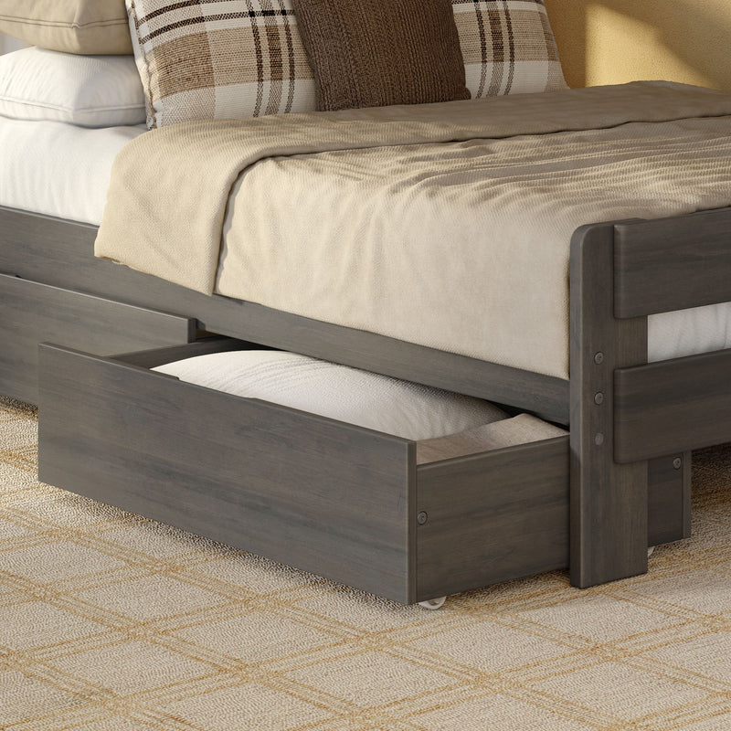Gray wooden trundle bed with under-bed storage drawer, beige textured bedding, neutral throw blanket and plaid and knit accent pillows