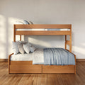 Modern solid wood bunk bed with blue-gray bedding and pillows, built-in under-bed drawers on hardwood floor in sunlit minimalist bedroom