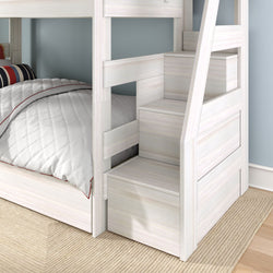 White wooden bunk bed with built-in storage stairs and drawers, lower twin bed with quilted white comforter and striped pillow in a children's bedroom