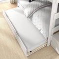 Underbed trundle mattress pulled out from whitewashed light wood bunk bed with quilted white duvet on beige rug — space-saving storage for kids' bedroom.