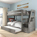 Gray wooden bunk bed with trundle and staircase in coastal kids' bedroom, white quilted bedding with red piping, striped pillows, and rustic oar wall decor on light blue wall