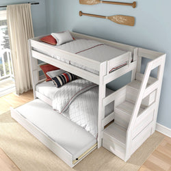 White wooden bunk bed with built-in staircase, pull-out trundle and storage drawers, white quilted bedding and striped pillows against a light-blue coastal bedroom wall with wooden oar decor