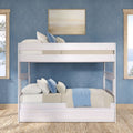 White wooden bunk bed in coastal-style blue bedroom with layered neutral bedding, blue and beige throw pillows, light-wood windows and natural jute rug