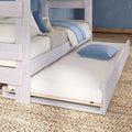 Whitewashed wooden bunk bed with pull-out trundle mattress, blue striped pillow on woven rug — space-saving kids bedroom furniture