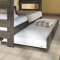 Trundle bed under a bunk bed with pull-out mattress and plaid pillow, dark wood frame and neutral bedding on a patterned rug