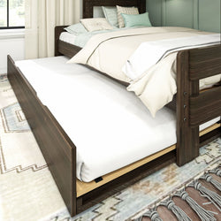 Dark wooden bed with pull-out trundle and cozy bedding in a bright bedroom setting.