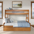 Twin-over-full wooden bunk bed, natural oak finish with blue bedding and storage trundle in a coastal-style bedroom with framed lake painting and large windows