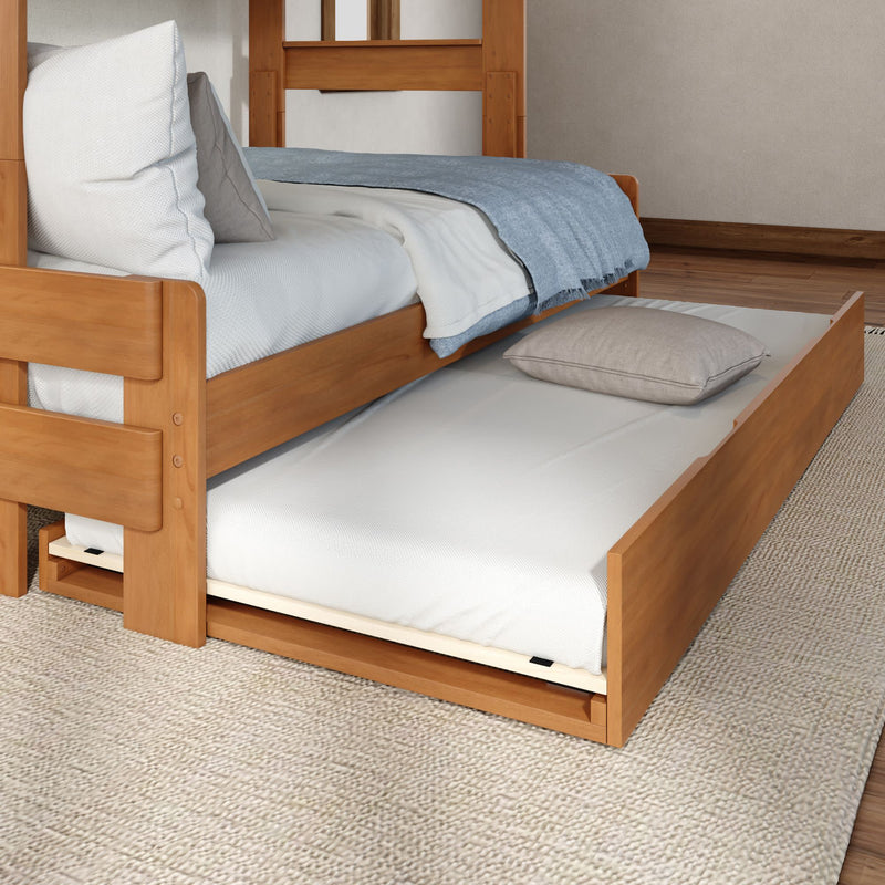 Solid wood trundle bed with pull-out mattress under a single wooden bed, white bedding and blue throw on a textured rug — space-saving guest bed solution