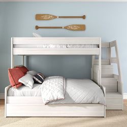 White wooden bunk bed with staircase and trundle in coastal kids bedroom, light blue wall with decorative wooden oars, quilted white bedding and red accent pillows
