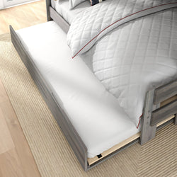 Gray wooden trundle bed pulled out beneath twin bed with white quilted bedding on natural rug — space-saving guest or kids storage bed