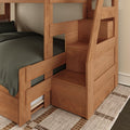Two-tier solid wood bunk bed with built-in staircase and hidden storage drawers in a natural finish, children's bedroom furniture with dark green bedding on a patterned rug