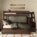 Dark walnut wooden bunk bed with staircase storage and green bedding in a neutral bedroom with mounted decorative oars