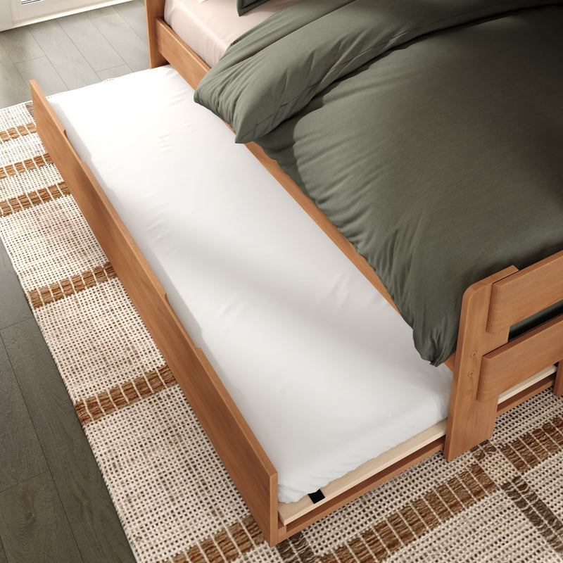 Wooden pull-out trundle bed with white mattress and green duvet on hardwood floor and woven rug