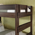 Dark walnut solid wood twin-over-twin bunk bed close-up showing sturdy guardrails and ladder with white and green bedding against a textured light-green wall