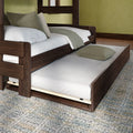 Dark walnut trundle bed with pull-out twin mattress, white quilt and green accent pillows on a textured area rug — space-saving modern bedroom furniture