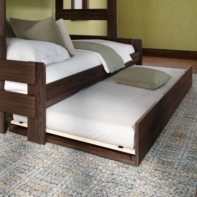 Dark walnut trundle bed with pull-out twin mattress, white quilt and green accent pillows on a textured area rug — space-saving modern bedroom furniture