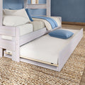 Whitewashed wood bed with pull-out trundle mattress, blue throw and striped pillow on woven jute rug