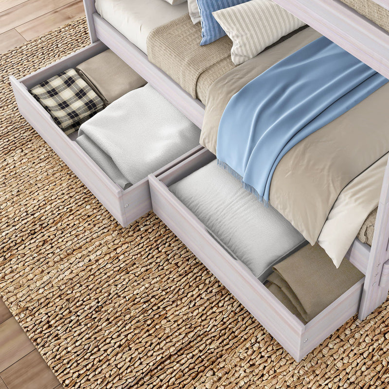 Light wood bed with pull-out underbed storage drawers filled with folded blankets, pillows and a blue throw on woven jute rug