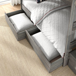 Gray wooden bunk bed with under-bed pull-out storage drawers holding white pillows and quilted white bedding on a beige rug — space-saving kids bedroom storage solution