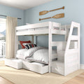 Whitewashed wooden loft bunk bed with built-in storage drawers and staircase in a coastal-style bedroom with light blue walls and decorative wooden oars.