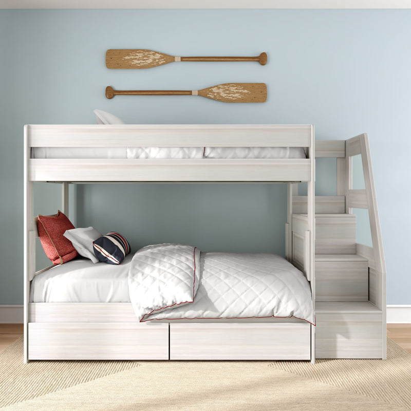Modern kids white wooden bunk bed with built-in storage stairs, quilted white bedding, navy and red pillows on a light blue wall with decorative wooden oars
