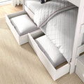 White wooden bed with two pull-out under-bed storage drawers holding pillows and white quilted bedding, space-saving bedroom storage solution