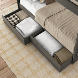 Gray wood platform bed with built-in under-bed storage drawers holding folded blankets, pillows, and linens in a neutral bedroom