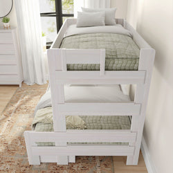 White wooden bunk bed with green quilts and white pillows, in a bright bedroom with a textured area rug and natural light from a large window.