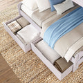 Light wood platform bed with under-bed storage drawers storing folded blankets and pillows, blue throw on neutral bedding