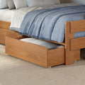 Light wood trundle bed with pull-out storage drawer, white bedding and blue woven throw blanket on a textured beige rug