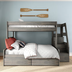 Gray wooden twin-over-full bunk bed with staircase, built-in storage drawers, white quilted bedding and red pillows in coastal blue kids' bedroom with decorative wooden oars