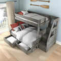 Gray washed wood twin-over-full bunk bed with built-in staircase and pull-out storage drawers, white quilted bedding and red nautical pillows in bright coastal bedroom