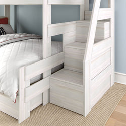 Whitewashed wooden bunk bed with built-in storage staircase and lower twin bed, white quilted bedding and blue wall