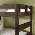 Close-up of dark walnut solid wood twin-over-twin bunk bed with safety guardrail, ladder posts and white mattress against a green textured bedroom wall