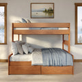 Natural wood bunk bed with built-in storage drawers, layered neutral pillows and blue linen throw in a sunlit rustic bedroom with framed lake artwork