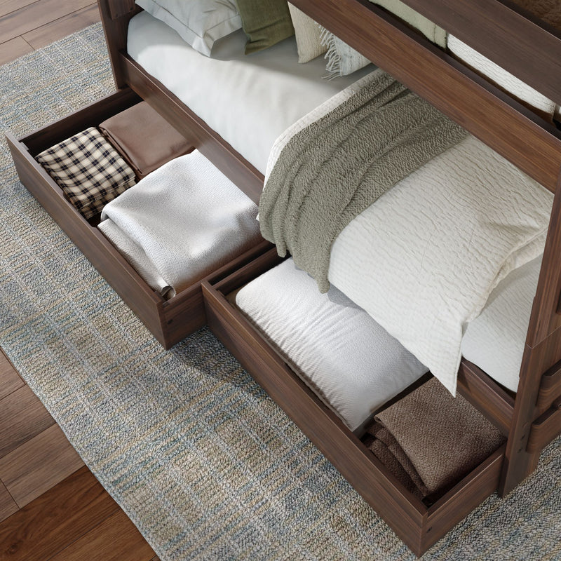 Under-bed storage drawers in a walnut wooden bed frame filled with neatly folded blankets, pillows and linens on a textured rug and hardwood floor — space-saving bedroom organization solution