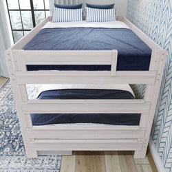 Whitewashed wooden twin-over-twin bunk bed with navy bedding and striped pillows in a coastal-style children's bedroom with hardwood floor and patterned wallpaper