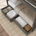 Wooden bed frame with under-bed storage drawers holding folded blankets and pillows, neutral beige bedding and plaid rug — space-saving bedroom organization solution