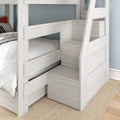 Whitewashed wooden twin-over-twin bunk bed with built-in storage staircase and drawers, quilted bedding, and natural fiber rug in a modern kids' bedroom