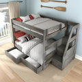 Gray weathered wood bunk bed with built-in staircase and pull-out storage drawers, white quilted bedding and red accent pillows in a coastal bedroom with paddles on the wall and balcony lake view
