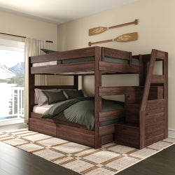 Dark walnut wooden bunk bed with staircase and built-in storage drawers in cozy lakeside bedroom featuring green bedding, decorative canoe paddles on the wall, large window with lake and mountain view, and plaid area rug