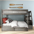 Gray wooden bunk bed with staircase and under-bed storage drawers, full lower bed and twin upper, white quilted bedding and red accent pillows against light-blue wall with wooden oars