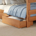 Solid wood bunk bed with pull-out trundle storage drawer in a modern bedroom, neutral bedding and pillows topped with a light blue textured throw blanket on a woven area rug