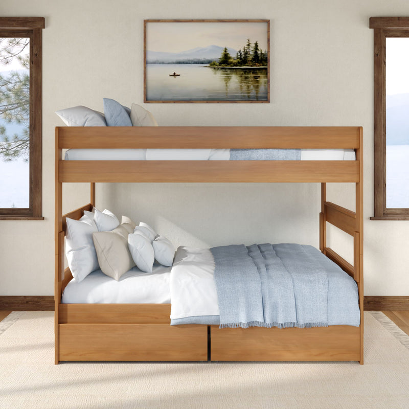 Solid wood twin-over-full bunk bed with under-bed storage drawers, light blue bedding and multiple pillows in a cozy lake-view bedroom with framed landscape art