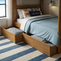 Wooden platform bed with two under-bed storage drawers open, light blue duvet, coastal "Sea Breeze" accent pillow and blue-striped rug