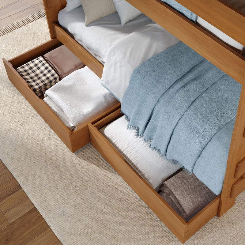 Wooden platform bed with pull-out under-bed storage drawers holding neatly folded blankets and pillows, blue throw — space-saving bedroom storage