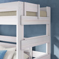 Whitewashed wooden bunk bed close-up with top guardrail and beige mattress, white and blue pillows on lower bunk against a blue textured wall — modern space-saving bunk bed