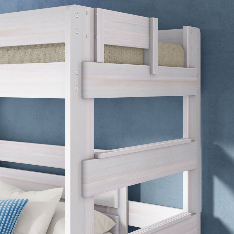 Whitewashed wooden bunk bed close-up with top guardrail and beige mattress, white and blue pillows on lower bunk against a blue textured wall — modern space-saving bunk bed