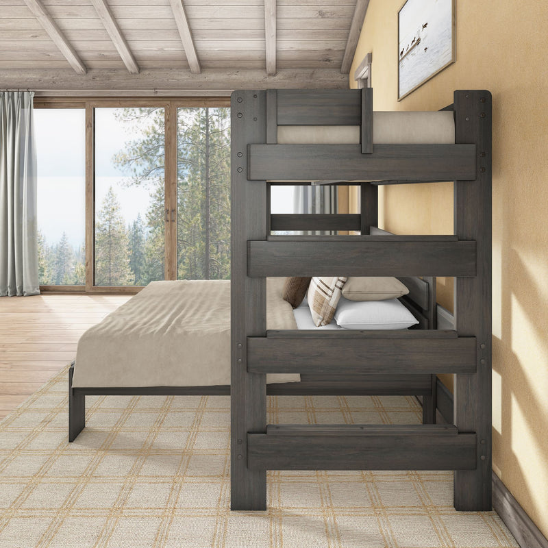 Rustic bedroom with dark wood bunk bed, beige bedding and plaid pillows beside floor-to-ceiling window overlooking a pine forest